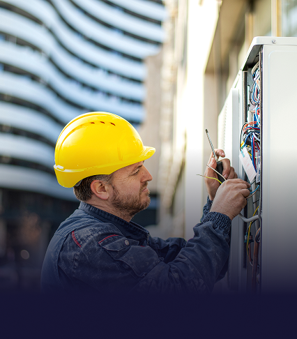 An electrician in a yellow hard hat working in an electrical panel
