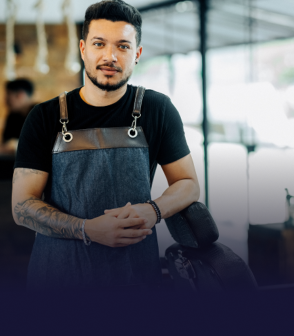 A barber stands with his hands folded, leaning on a barber chair in a salon